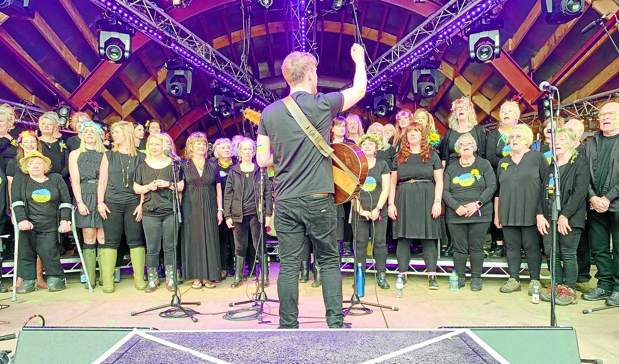 A tall white poster with a gray banner top and text reading "Discover Our Community Choir" stands alongside a white donati...