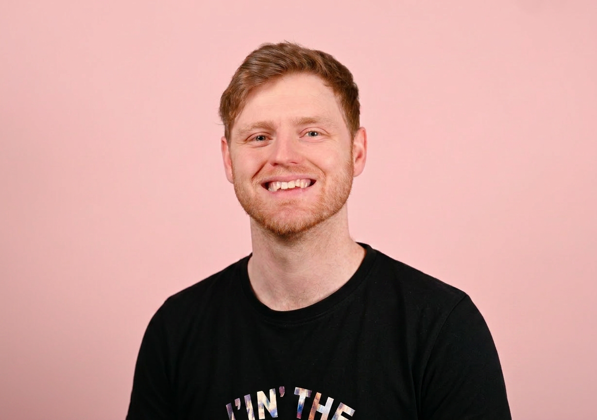 Smiling young man wearing denim shirt over black t-shirt against pink background